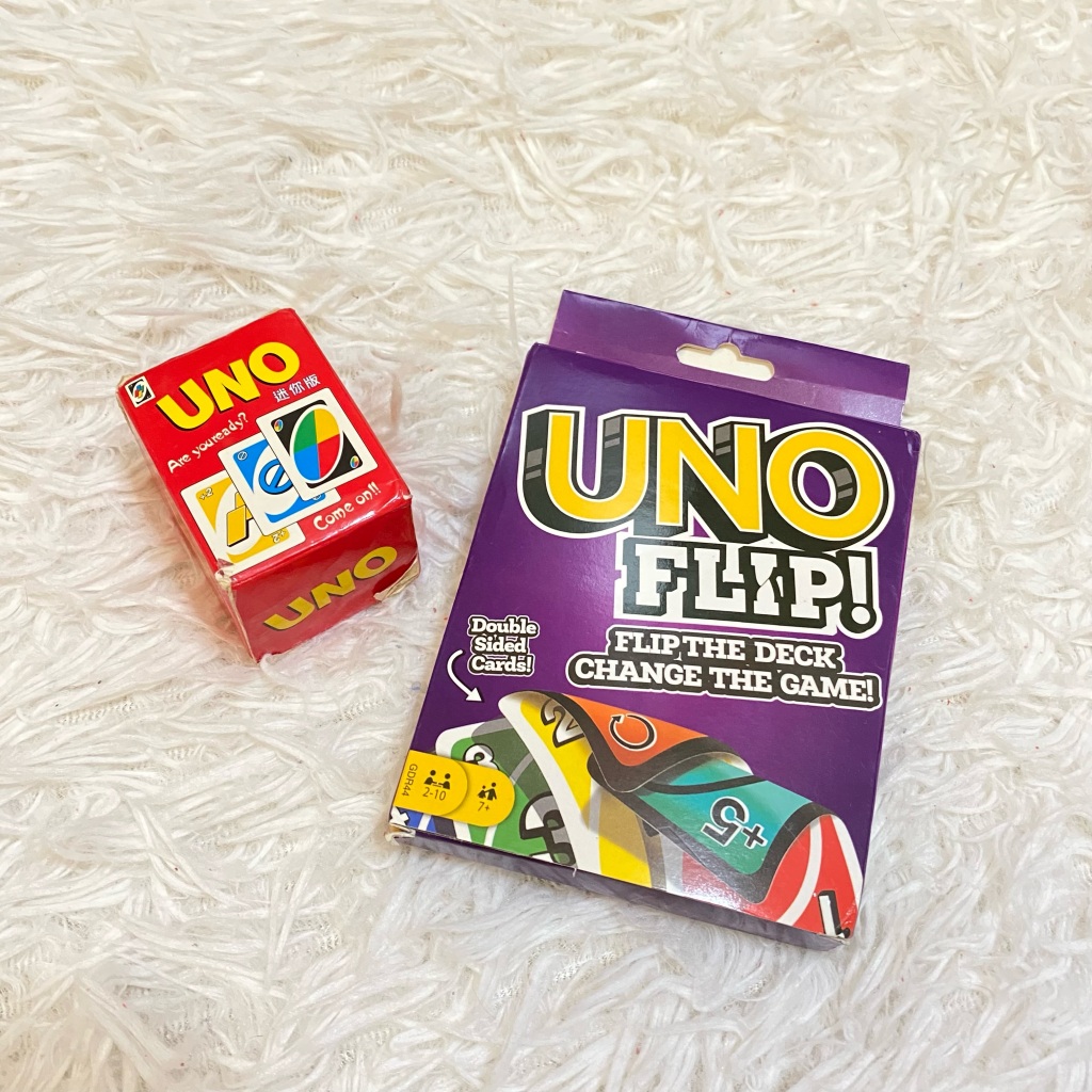 The packaging of Uno and Uno Flip!, two card games, placed side by side on a white carpet.